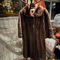 Front view of vintage brown fur coat hung on hanger, showing full length and wide collar