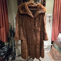 Front view of vintage brown fur coat hanging on a wooden hanger, showing length, lapels, and buttons.