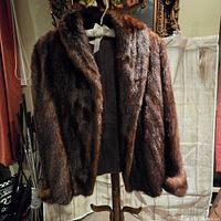 Full front view of the brown fur coat hanging on a stand showing collar and cuffs.