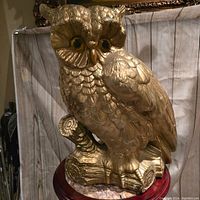 Front and right side view of the gold owl piggy bank showing detailed feather texture and yellow eyes. Visible chip on ear.