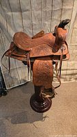 Right side angled view of western leather saddle on stand showing overall condition, tooling, and suede seat.