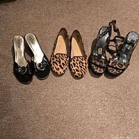Three pairs of women's shoes on carpet: black slip-ons with buckle, leopard print flats, and black animal print strappy heels.