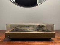Side front view of the turntable with dust cover closed, showing wood finish and Dual logo.