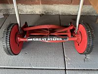 Close-up of red reel mower blade and wheels with Great States branding on the axle.