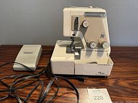 Full view of Janome serger sewing machine with attached power cord and separate electronic foot pedal on wooden table.