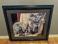 Full shot of framed oil painting showing entire artwork and frame against wall and floor.