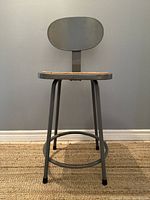 Front view of the mid century industrial metal stool with removable backrest showing the metal frame, wooden seat, and oval backrest.