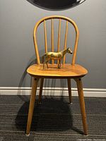 Full view of mid-century Danish wooden chair with brass horse figurine on seat