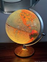 Illuminated globe showing North and South America with warm orange light internal illumination, wooden base, and metal armature