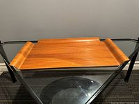 Full view of mid century modern teak tray with curved side handles, placed on glass table.