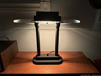Postmodern 1980s Robert Sonneman style table lamp illuminated, showing the top clear oval textured glass diffuser and dual black cylindrical supports on a rectangular base with dimmer knob.