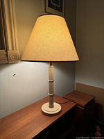Postmodern bamboo-style table lamp lit on a wooden surface, showing its bamboo-inspired base and a light beige lampshade.