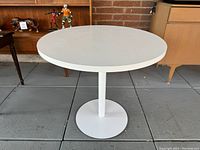 Front view of the round white bistro table with cylindrical pedestal base.