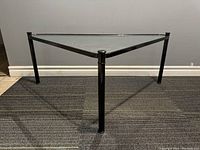 Front angle view of the triangular coffee table showing the steel legs and glass surface.