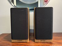 Front view of the pair of Tannoy Mercury M2 bookshelf speakers showing cherry wood casing and black fabric grilles with Tannoy logos at bottom.