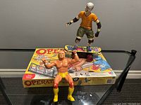 Wrestler, skateboarder figures and Operation game box on glass table
