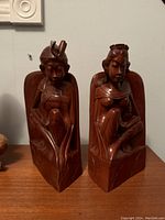 Pair of vintage Balinese hand carved wood bookends showing two seated figures, photographed on a wooden surface against a wall.