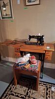 Full view of antique Singer treadle sewing machine in wooden cabinet with cushioned stool and sewing notions on stool