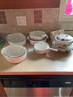 Photo of various CorningWare and ceramic bakeware on countertop, showing multiple dishes with clear glass lids and floral and fruit designs.