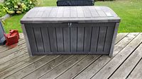 Front view of grey plastic outdoor deck storage box with domed lid and wood panel effect shows overall condition and latch area.