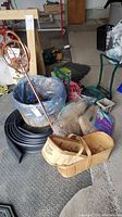 Photo showing copper sprinkler, wooden baskets, garden edging coils, burlap sacks, and bird feeder among other garden supplies on garage floor.