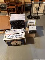 Boxes containing different sets of glassware, including Crown Royal and other brands, stacked in a basement setting.