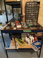 Photo of work table with various tools, bottles, cords, and other hardware supplies on and under the table