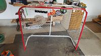 Full view of the Winnwell red metal framed hockey net with white netting in a garage setting.