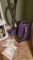 Kenmore purple canister vacuum and extra vacuum bags on tiled floor.