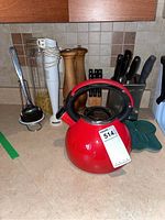 Red metal kettle, white Braun hand mixer, wooden salt and pepper shakers, kitchen knives, green dish, metal ladle, glass jar with pasta visible on kitchen counter