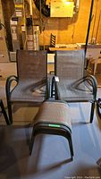 Two metal framed patio chairs with beige mesh seats and armrests shown with matching ottomans in front.