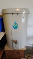 Front view of beige plastic rain barrel with spigot tap and water-drop logo