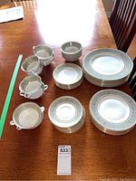 Full set arranged on table showing stacked dinner plates, lunch plates, bread plates, small bowls, cups, and saucers with gold and blue English Renaissance border pattern