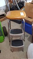 Front view of vintage step ladder stool showing cushioned tan seat and two metal steps with black rubber tread.