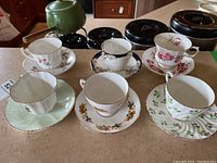 Overview of six bone china tea cups and matching saucers with various floral patterns and gold trims on countertop