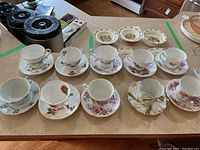 Overview of all 10 tea cups and matching saucers arranged on table showing various floral patterns and styles.