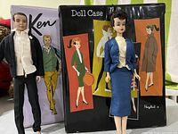Ken doll standing beside Barbie doll with their illustrated cases