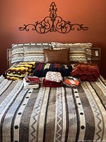 California king bed with comforter set, pillows arranged at head, three folded afghans and folded pillow cases on bed, metal scroll wall decor above headboard.