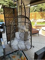 Front view of hanging egg style patio chair with beige cushions and metal stand in outdoor setting.