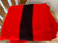 Folded red wool blanket with a single vertical dark stripe visible on top, showing the soft and thick wool texture.