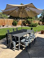 Photo showing the full patio dining set with shadows cast on the stamped concrete patio, umbrella open, and eight metal chairs arranged around the rectangular metal table.