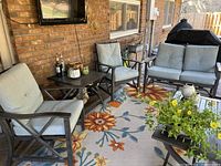 View of full set showing one outdoor metal frame sofa and two matching armchairs with light blue cushions on a patio rug with floral design.