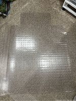 Clear plastic chair mat with dimples on the underside, placed on carpeted floor, showing transparency and wear marks.