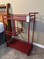 Front side view of red metal cart showing top shelf, side basket, and wheels.
