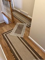 Two narrow beige and brown runners placed on hardwood floor near stairs and hallway, showing striped rectangular borders.