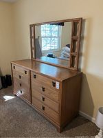 Photo of vintage wooden dresser with mirror attached, showing six drawers and metal handles, wooden frame mirror with decorative cutouts on sides.