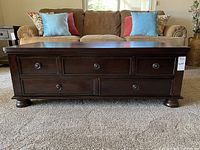 Front view of the dark stained wood coffee table with five drawers and round knobs. Shows scratches and overall wear on the wood surface.