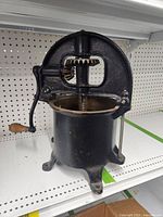 Full view of black cast iron antique sausage stuffer showing base, hand crank, and gear housing.