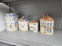 Front view of four Avon townhouse ceramic canisters displayed on a metal shelf, showing detailed hand-painted facades and roofs.