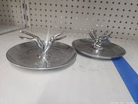 Two chrome ashtrays with double bird figurines positioned side by side on a shelf.